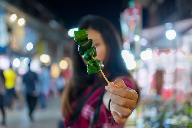 Close-up of woman holding food in skewer at night