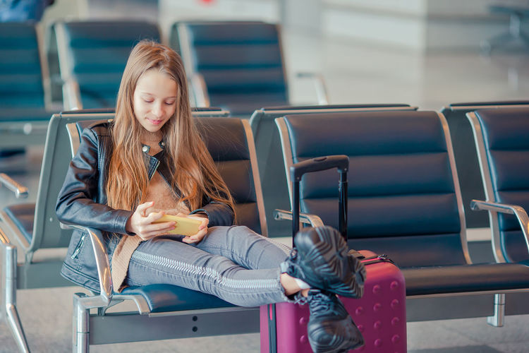 Girl using mobile phone while sitting at airport