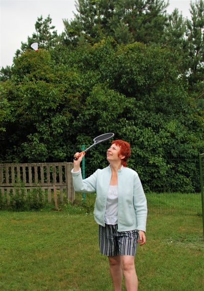 Smiling mature woman playing badminton on field in park