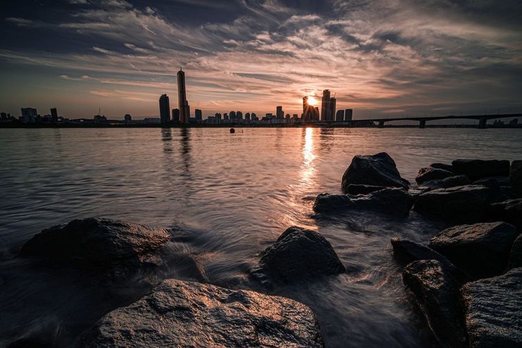 Scenic view of sea by buildings against sky during sunset