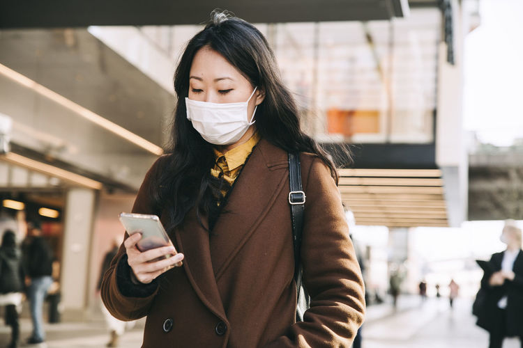Woman walking in street with face mask using smartphone