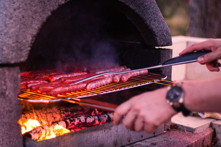 Cropped image of person hand cooking sausages on barbecue grill