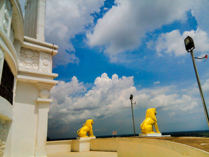 Yellow lion statues at shanti stupa at dhauligiri against cloudy sky