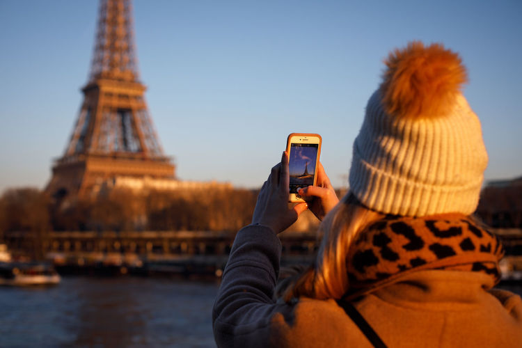 A young adult takes an iphone picture of the eiffel tower in paris.