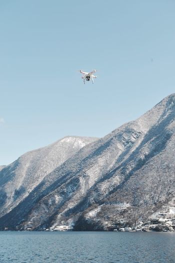 Low angle view of drone airplane flying over lake by mountains against sky
