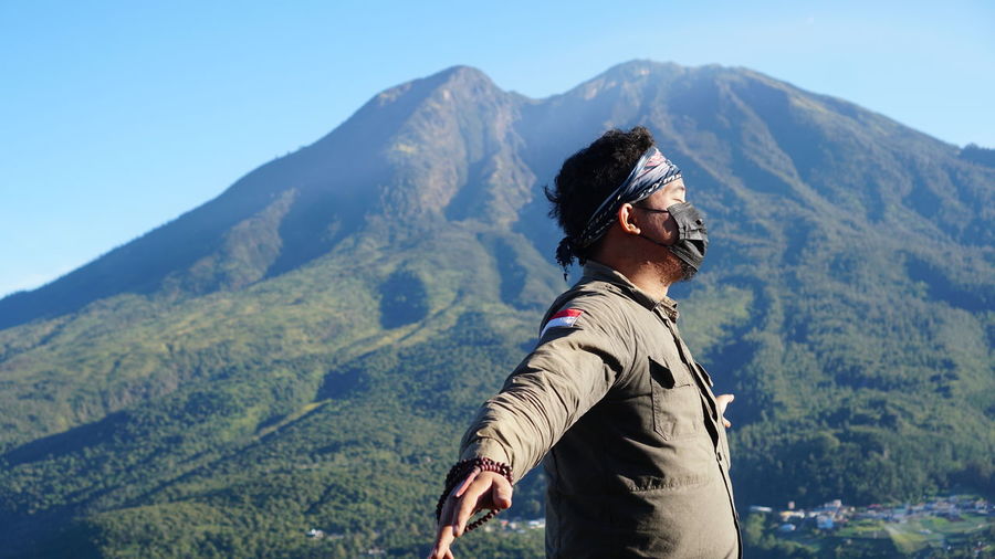 Side view of man standing on mountain against sky