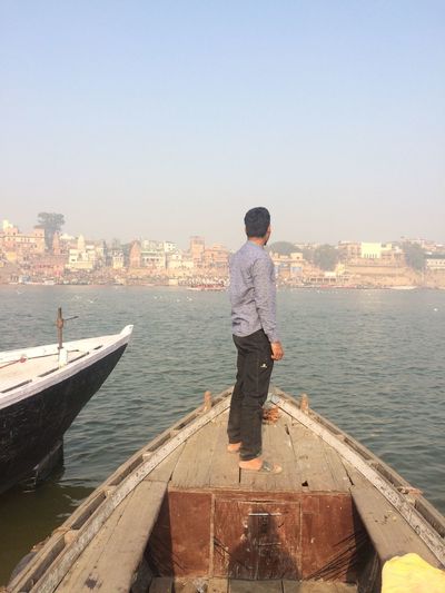 Rear view of man standing in sea against cityscape