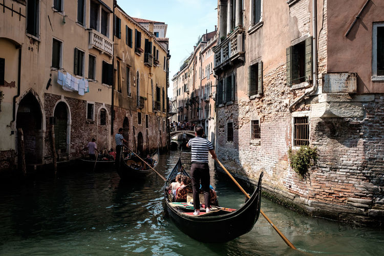 Rear view of gondolier in gondola at canal amidst old buildings