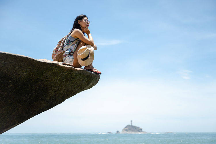 Low angle view of young woman sitting on sea against sky