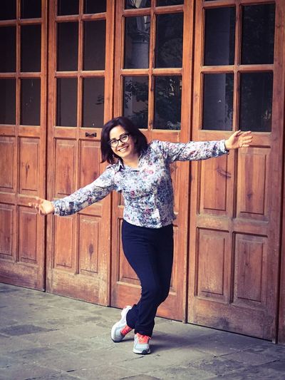 Portrait of happy young woman with arms outstretched by wooden doors