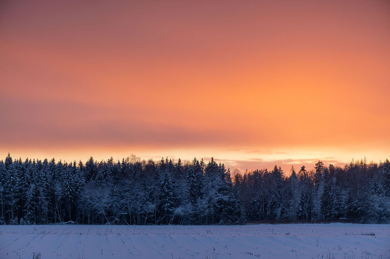 Snow covered land against sky during sunset