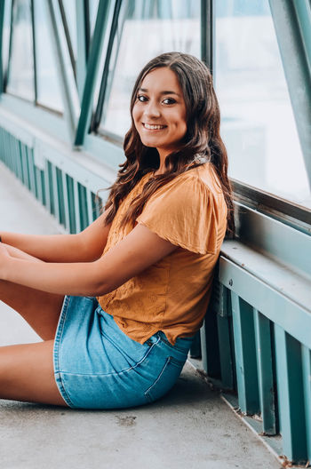 Portrait of a smiling young woman sitting on footbridge
