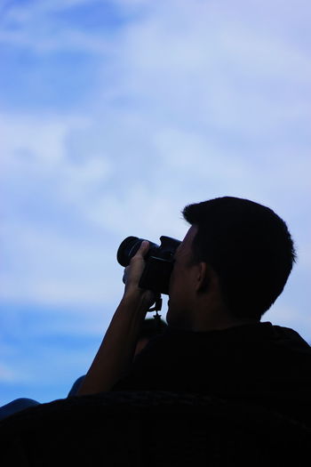Low angle view of man photographing against sky