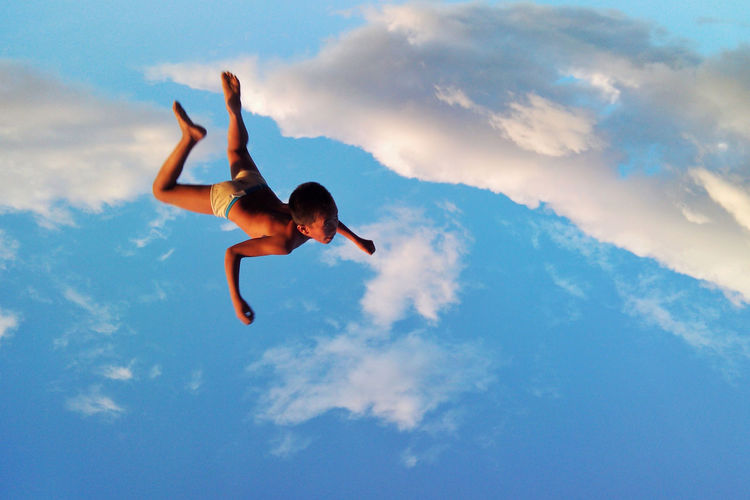 Low angle view of woman jumping against cloudy sky