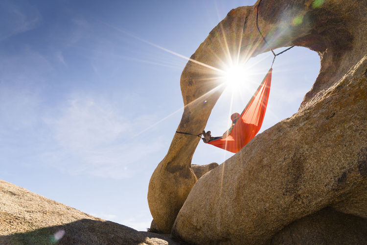 Low angle view of woman relaxing on hammock hanging from rock formation