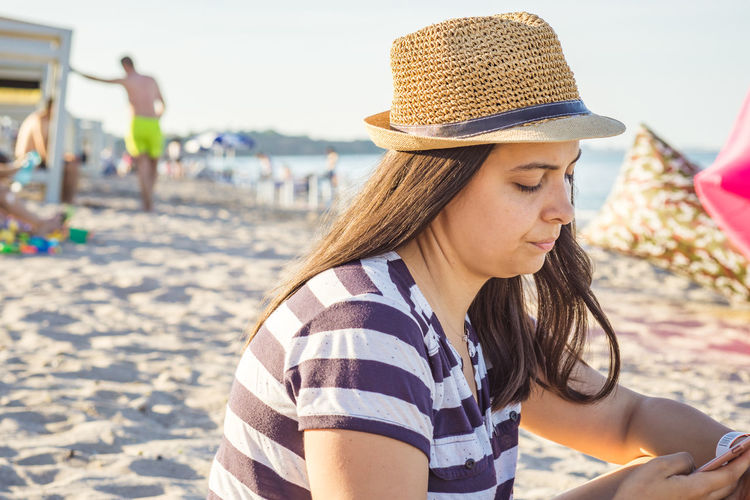 Young woman wearing hat using mobile phone at beach