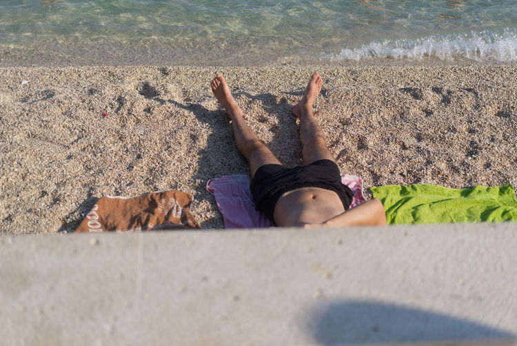 Low section of person lying on sand at beach
