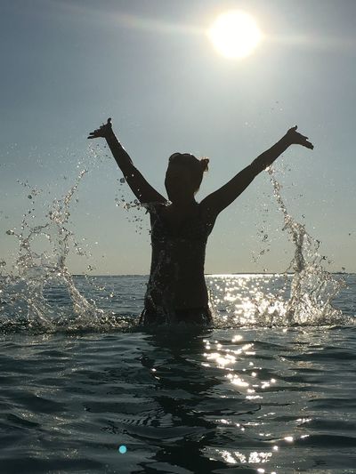 Silhouette of woman splashing water in sea against sky