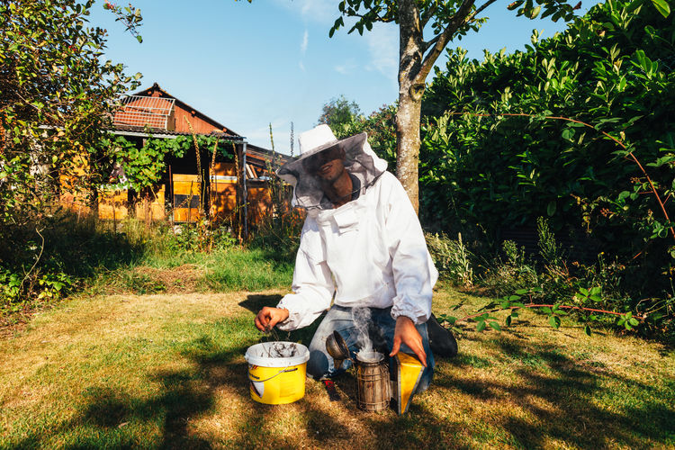 Beekeeper kneeling by equipment on grass