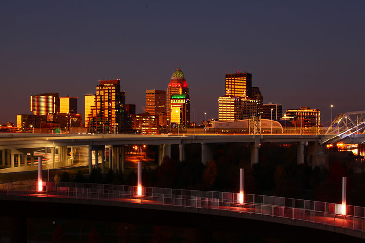 Illuminated modern buildings by river against sky at night