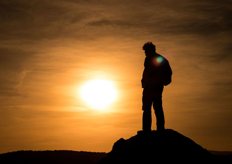 Travelling - silhouette man standing on rock against sky during sunset