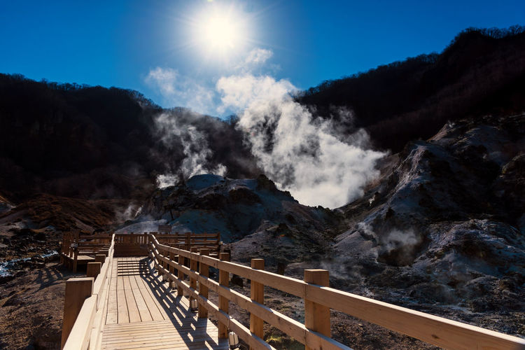 Jigokudani hell valley walking trail or wood footpath with sulfur misty, blue sky, and sunbeam