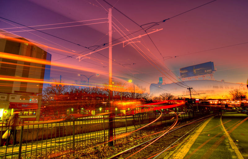 Illuminated railroad tracks in city against sky at sunset