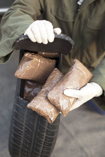 Low section of man holding cocaine parcels in tire