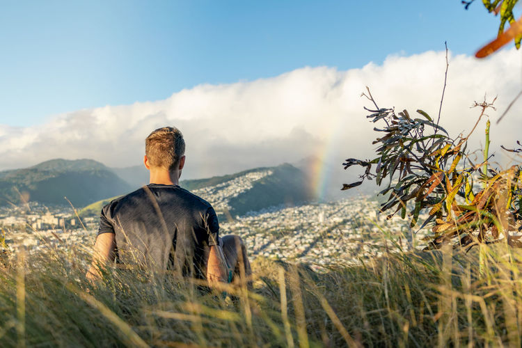 Rear view of man looking at rainbow and mountains against sky