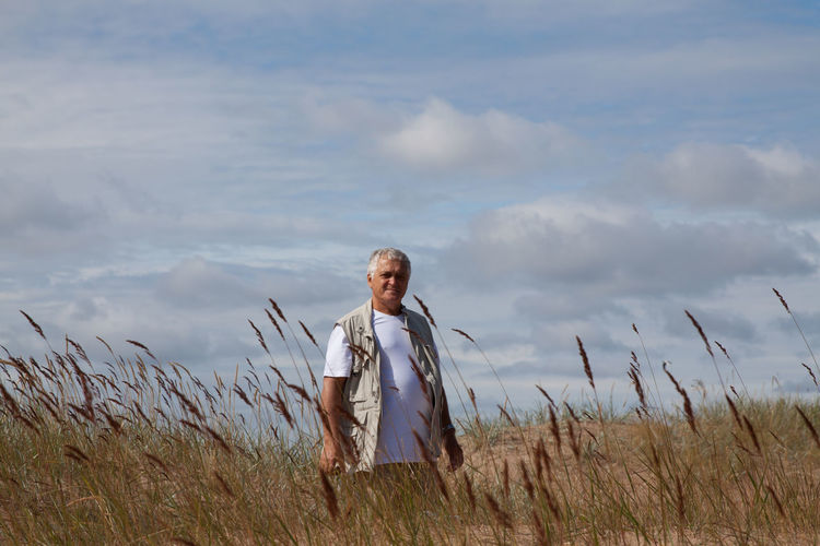 Mature man standing on field against sky