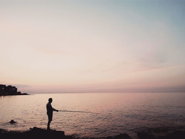 Man holding fishing rod while standing on rock at shore