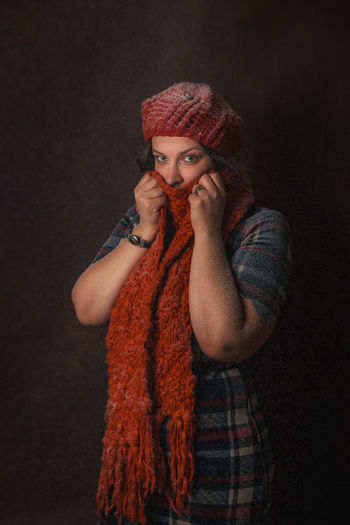 Portrait of young woman covering face with scarf while standing against black background