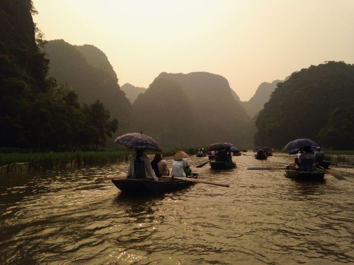 People sitting in boat at river against mountains