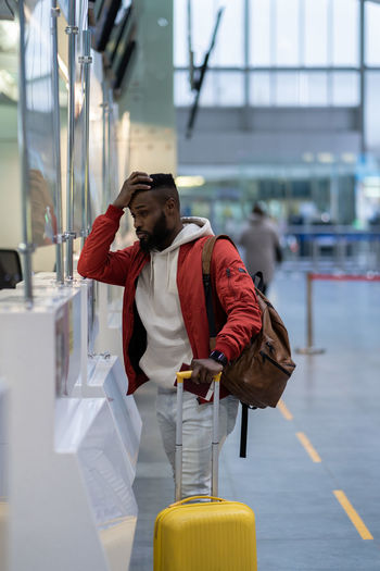 Upset african man standing at check-in counter in airport, being sad about moving away