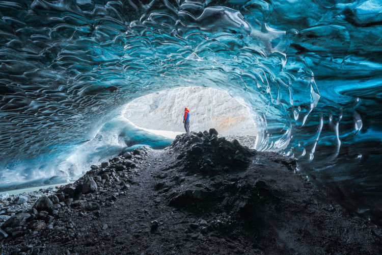 Tourist in outerwear standing near uneven holes in ice surface while exploring cave in vatnajokull glacier on winter day in iceland