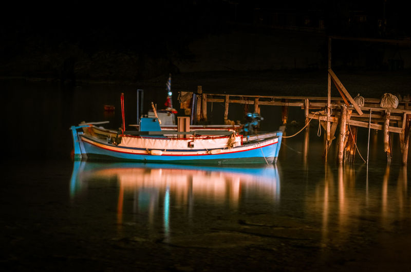 Boats moored in illuminated water at night