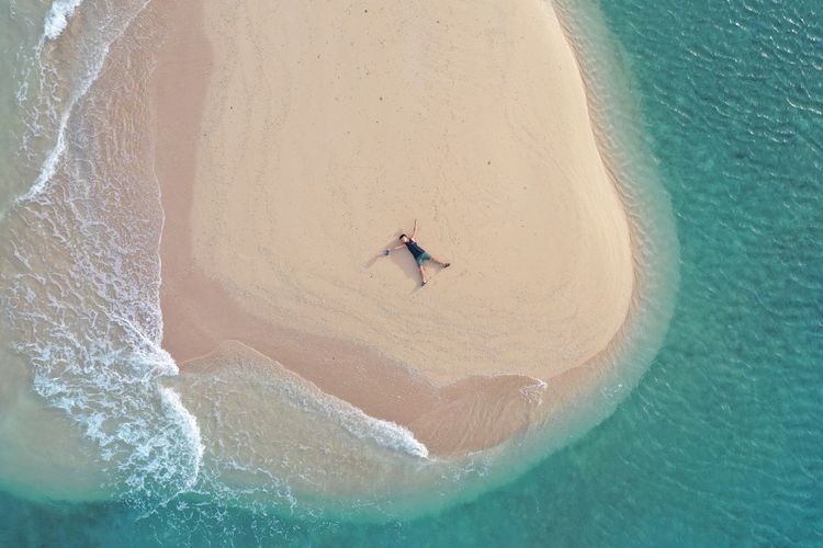 Aerial view of man lying on sad amidst sea