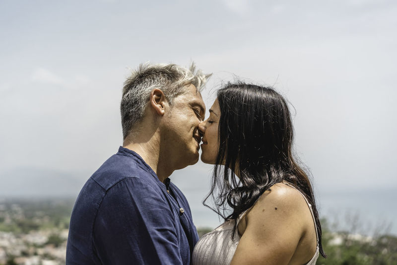 Side view of couple kissing against sky