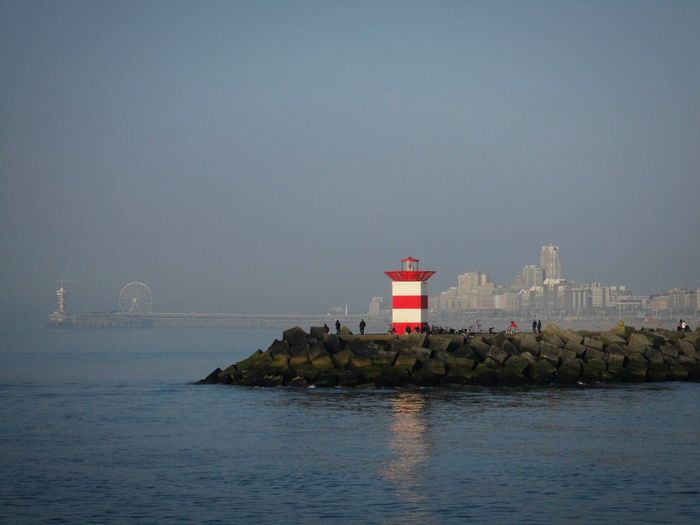 Lighthouse by sea against buildings against clear sky