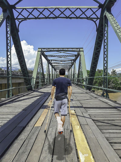 Rear view of disabled man walking with canes on footbridge