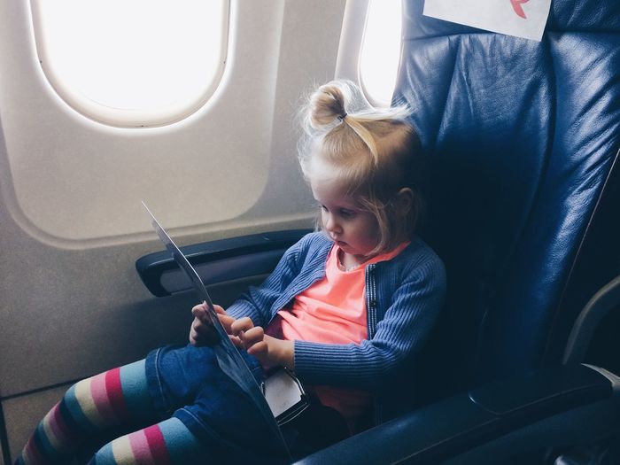 Girl reading chart while sitting by window in airplane