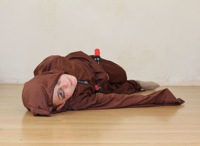 Portrait of boy wearing brown costume lying on hardwood floor at home