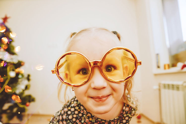 Little girl wearing gold masquerade glasses smiling, fooling around. happy 2021
