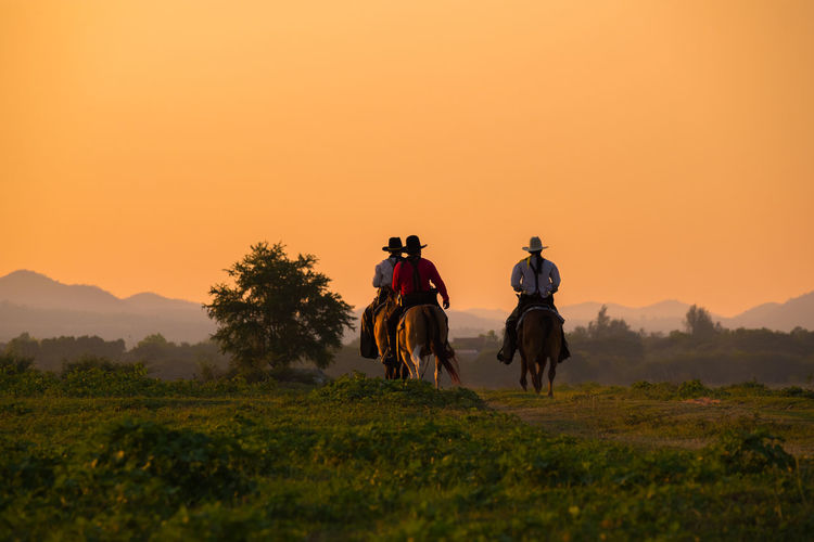 People riding horse on field against sky during sunset