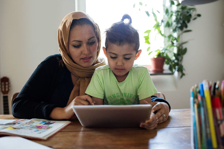 Mother assisting son in using digital tablet while studying at home