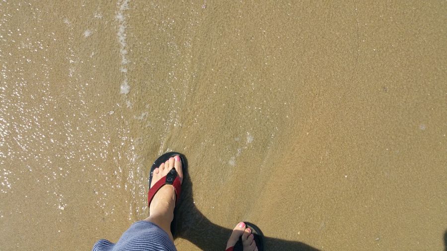 Low section of woman in red flip flops standing on wet sand beach