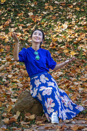 Full length of smiling woman sitting amidst autumn leaves