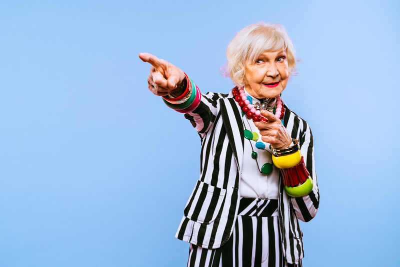 Senior woman pointing away against blue background