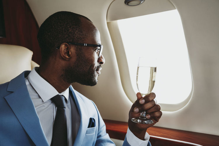 Young businessman with champagne looking through window in private jet