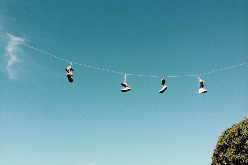 Low angle view of shoe pairs hanging on rope against sky
